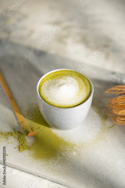 Fototapeta Organic green matcha tea with milk. Matcha powder and tea drink in a bowl. Chasen bamboo whisk for brewing matcha tea top view on white background with beautiful shades. Copy space.