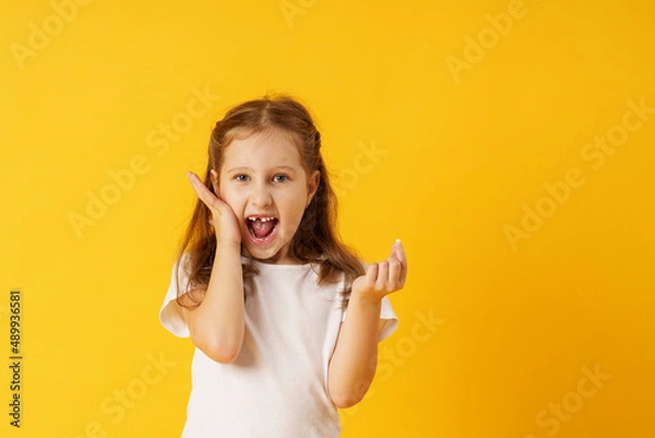 Fototapeta cute smiling preschool girl holds her first fallen baby tooth in her hand while standing on yellow background. growing permanent tooth is in the open mouth. . The concept of hygiene of baby teeth.