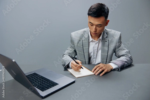 Fototapeta manager sitting at a desk in front of a laptop work writing in a notebook executive