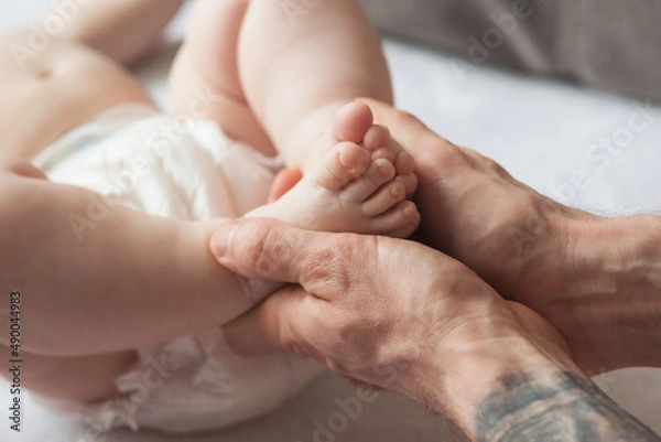 Fototapeta Dad holds the legs of a newborn. Happy parenting. The concept of education and care. Paternity. father's day