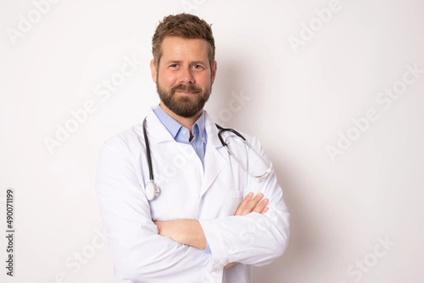 Fototapeta Young smiling male doctor posing with arms folded isolated on white background with copy space on the right side