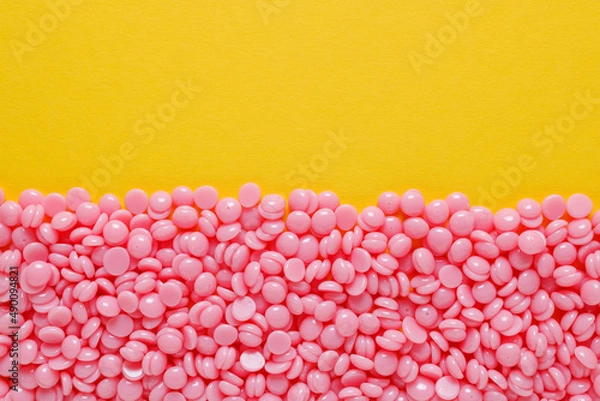 Fototapeta Beautiful pink depilatory wax granules on a yellow background. Epilation, depilation, unwanted hair removal. Top view. Place for text.