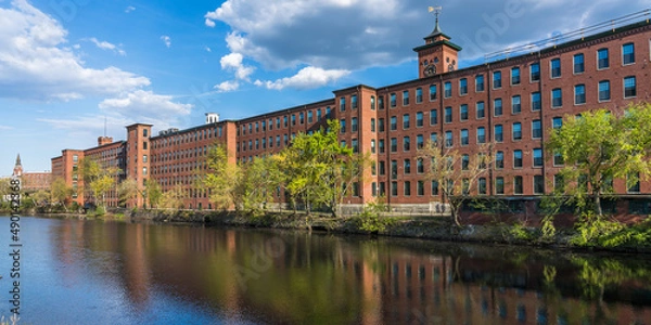 Fototapeta Historical building of a cotton factory with a clock tower in an old industrial park  on Nashua River in May. Nashua, New Hampshire, USA