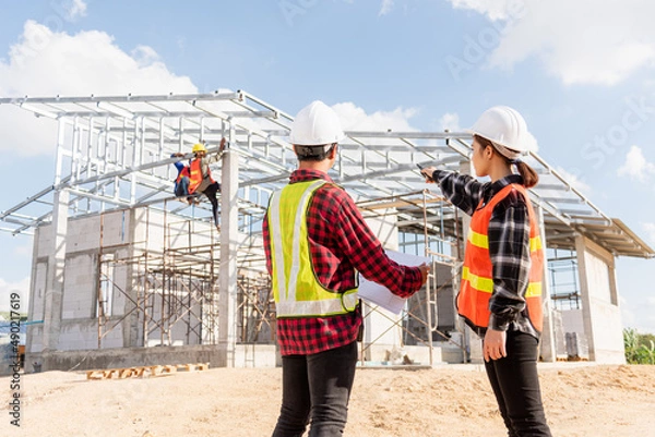 Fototapeta Back two architect and client discussing help create plan with blueprint home building at construction site. Asian engineer foreman worker man and woman meeting talking on drawing paper project