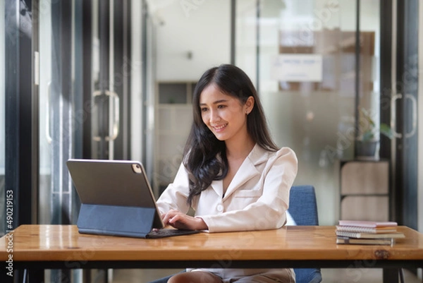 Obraz Confident asian business woman using computer tablet while sitting in bright modern office.