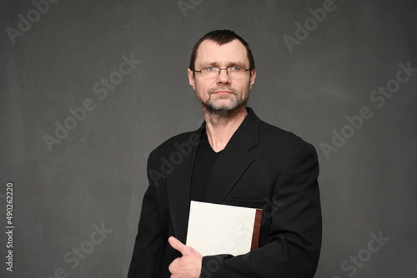 Fototapeta A businessman in a jacket looks at the camera with a folder in his hands. Portrait on a gray background in the studio