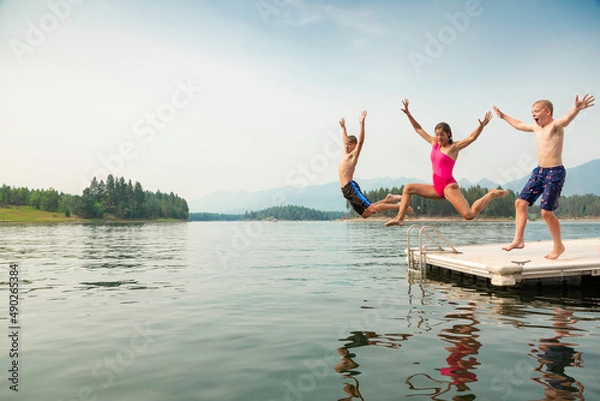 Fototapeta Group of kids jumping off the dock into the lake together during a fun summer vacation.