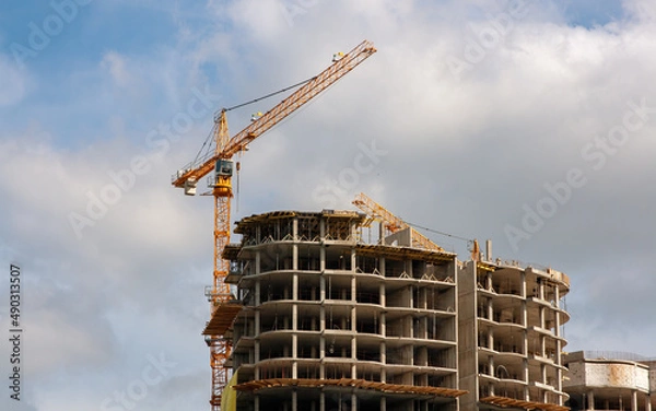 Fototapeta Construction. A construction crane and a building under construction. Sky. The clouds