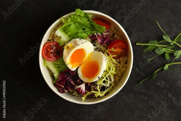 Fototapeta Healthy bowl with poached egg, bulgur, tomatoes and lettuce. on a dark background in an eco paper box. Healthy food delivery concept.