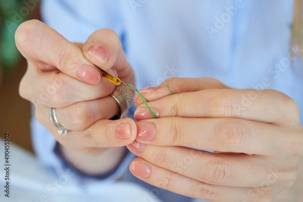 Obraz Close-up of female hands inserting a green thread into a needle