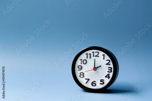 Fototapeta Black alarm clock isolated on blue background. The clock set at 2 o'clock.
