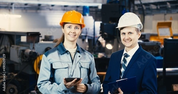 Fototapeta A portrait of an industrial man and woman engineer with tablet in a factory, working.