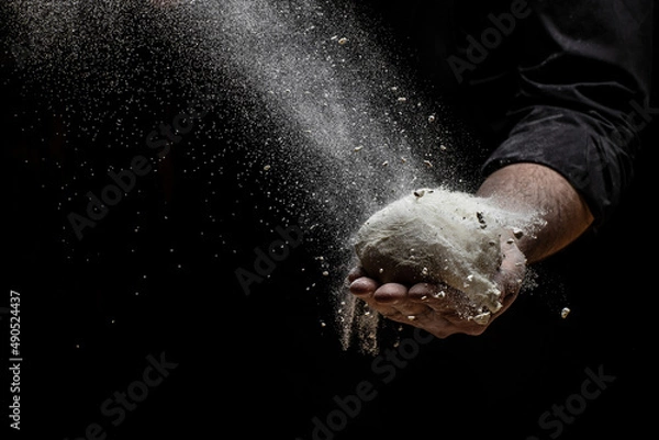 Fototapeta Beautiful and strong men's hands knead the dough from which they will then make bread, pasta or pizza. A cloud of flour flies around like dust. Food concept.
