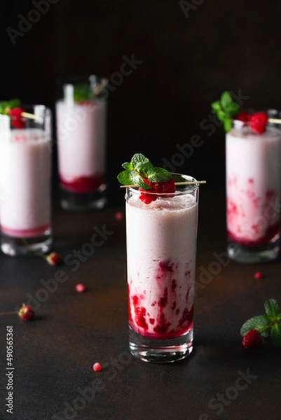 Fototapeta Raspberry milkshake or smoothie in a glasses decorated with mint and raspberries on a black background.