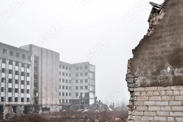 Fototapeta A broken brick wall in close-up against the ruins of a building and a gray sky in the fog. Background