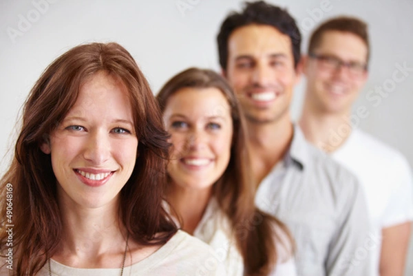Fototapeta Leading her team to success. Portrait of a group of young smiling business professionals standing in a row.