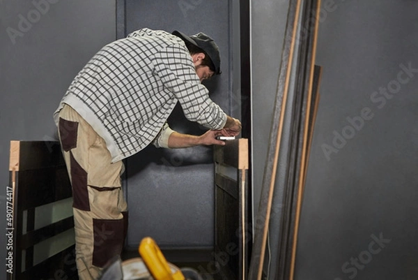Fototapeta Preparing the door for installation. A man installs a door handle