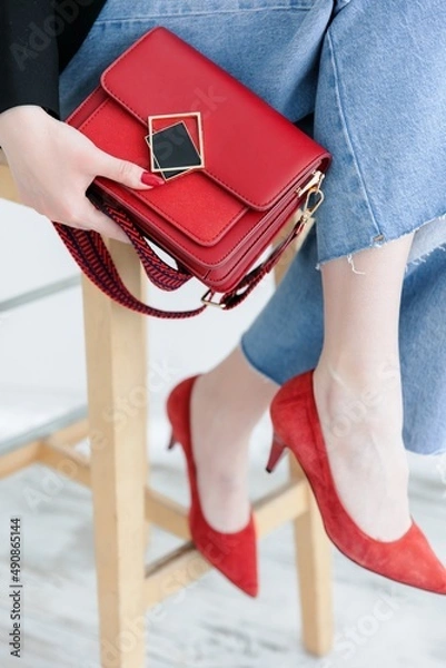 Fototapeta Small red handbag. Fashionable women's leather clutch bag with a fabric strap in the tone of the shoes. Girl . Traditional clutch bag with brooch. bag made of fine red genuine leather. Front view. 