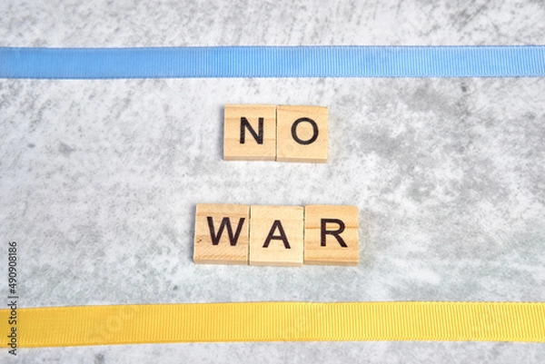Fototapeta phrase no war is laid out of wooden squares on a gray background with flag of ukraine with blue and yellow ribbon. Concept of peace, war in Ukraine