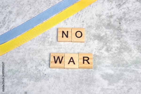 Fototapeta phrase no war is laid out of wooden squares on a gray background with flag of ukraine with blue and yellow ribbon. Concept of peace, war in Ukraine