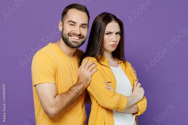 Fototapeta Young smiling displeased sad couple two friends family man woman together in yellow casual clothes try to hug offended girlfriend after argument isolated on plain violet background studio portrait.