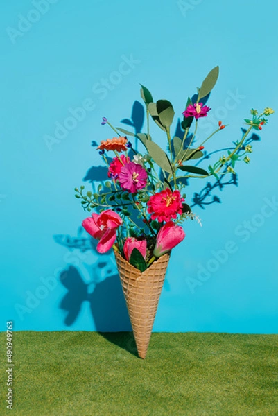 Obraz Ice cream cone with various field fresh flowers against blue wall and grass background. Creative natural summer dessert food concept. Spring bloom or love gift idea.
