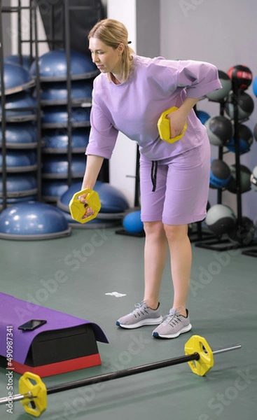 Fototapeta Woman holding a lightweight disk for working out arms and triceps in gym. Exercising and workout for weight loss and losing body fat.