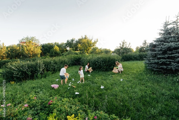Fototapeta A group of adults and children together at sunset is engaged in garbage collection in the park. Environmental care, waste recycling. Sorting garbage.