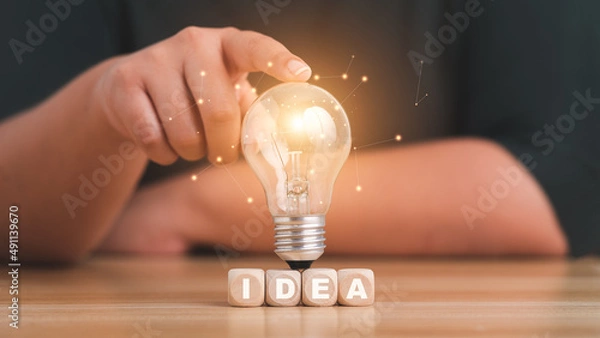 Fototapeta idea concept with innovation and inspiration.Female hand holding a lightbulb light bulb on wood block with Word Ideas.