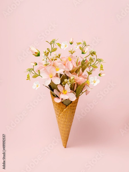 Obraz Ice cream cone filled with fresh flowers and leaves on pastel pink background. Creative floral spring bloom natural concept. Minimal summer dessert still life abstract idea.