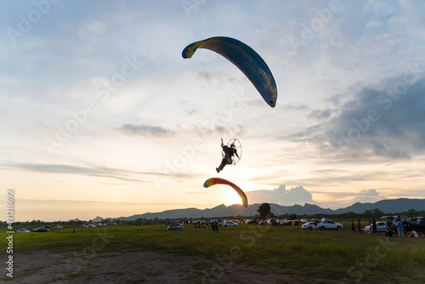 Fototapeta paraglider fly with paramotor flying in the air on a sunset with an Mountain and horizon in the background with a giant sun