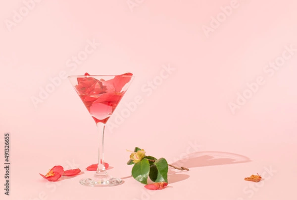 Fototapeta Martini glass and camellia flower on pink pastel background. Minimal party concept. Wedding day or love concept. Spring composition. Top view, copy space.