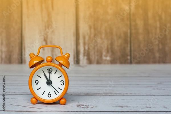 Fototapeta Orange alarm clock isolated on wooden desk. The clock set at 11 o'clock.