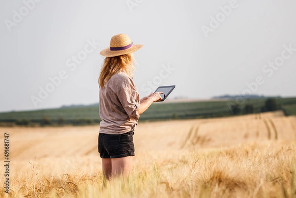 Fototapeta Farmer standing in barley field and examining quality of produce before harvest. Woman using digital tablet for smart farming