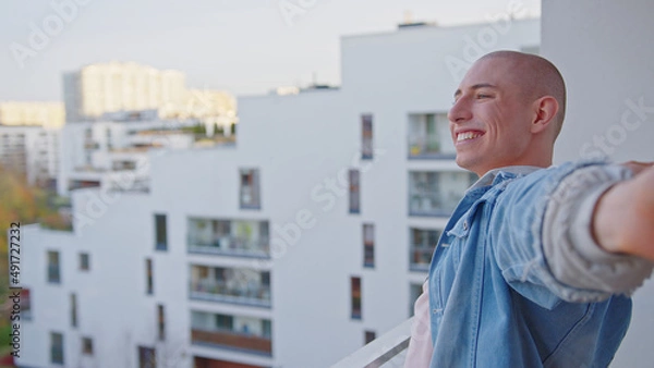 Fototapeta Happy caucasian queer non-binary person standing on balcony and smiling. High quality photo