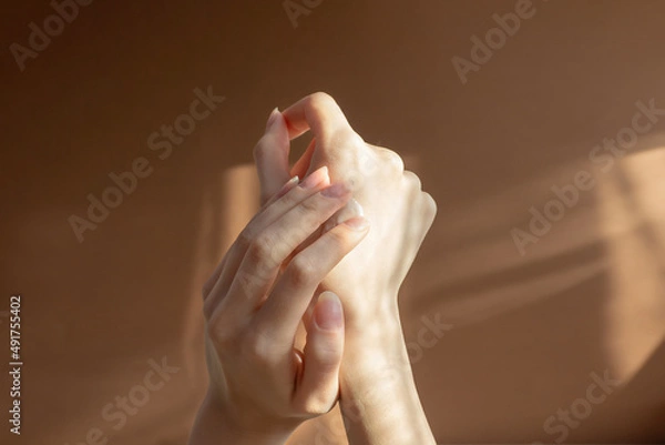 Obraz Beautiful female hands apply cream, lotion to skin. Close-up, beige background with striped shadow. Concept of care and beauty