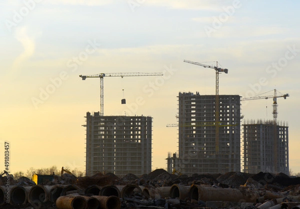 Fototapeta Construction site with buildings construction on sunset. Tower cranes in action. Housing renovation and real estate. Crane during formworks. New Housing and residential homes construction.