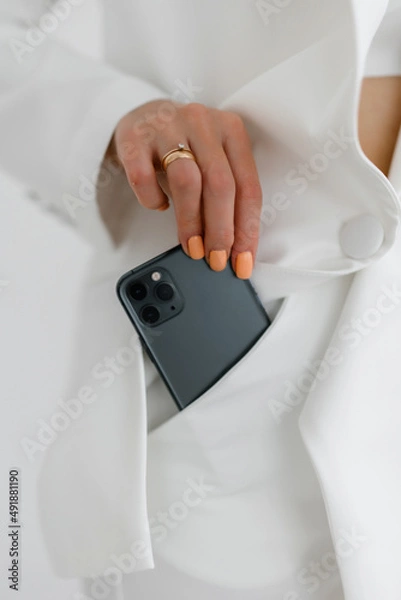 Fototapeta Girl pulls out a fancy green mobile phone from her white trouser pocket. 
Girl holding smartphone in trouser pocket. At close range. Technology. Modern, casual style.