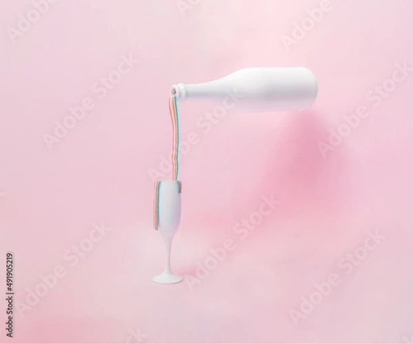 Fototapeta White champagne glass and bottle with colorful rainbow chewing gum how they spill on a pink pastel background.