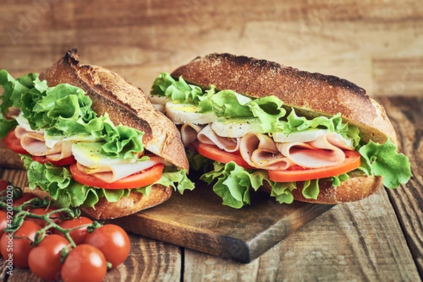 Obraz Two fresh sandwiches with ham on wooden table. Sandwich with ham tomato salad and mozzarella cheese on wooden table. Sandwich close up.