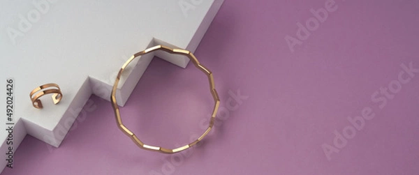 Fototapeta Panorama of Zig zag shape bracelet and golden ring on white geometric podium on pink background with copy space