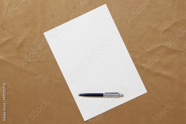 Fototapeta Template of white paper with pen lies diagonally on light brown cloth background. Concept of business plan and strategy. Stock photo with empty space for text and design.