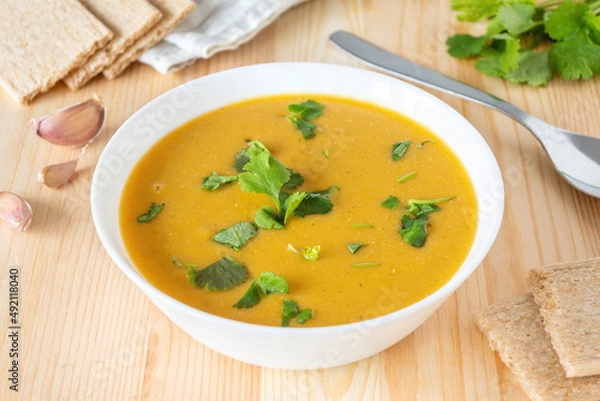 Fototapeta Veggie red lentil creamy soup in white bowl on wooden table. Homemade vegan lunch with crispbread.