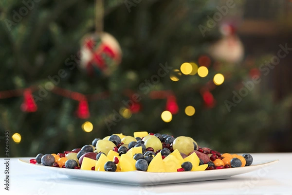 Fototapeta Mixed fruit salad on a white table with Christmas tree background
