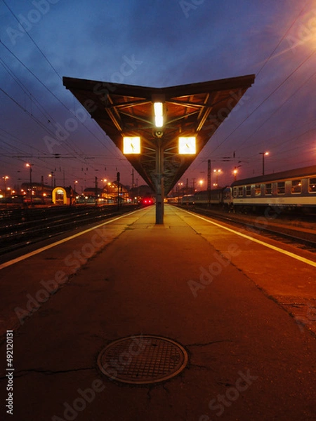 Fototapeta Railway platform with clock and a manhole in night city lights background