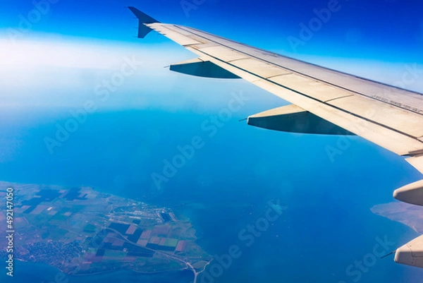 Fototapeta View from the airplane window at a beautiful blue clear sky, earth, sea and the airplane wing