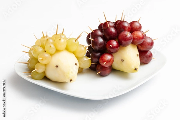 Fototapeta Hedgehogs made of fruits. Pear and grapes on a plate.