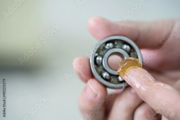 Obraz Worker use finger to put lithium grease into small bearing at laboratory. Yellow transparance grease on the finger. Testing and service concept. Preventive maintenance and checking bearing damage .
