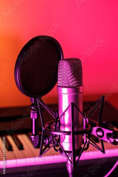 Obraz Close up of microphone with pop filter in front of piano keys with purple, pink, and orange ambient lighting.