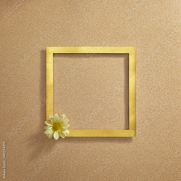 Fototapeta In the corner of the golden frame is a white daisy flower on a sandy background. Text space. Top view. Minimal style.